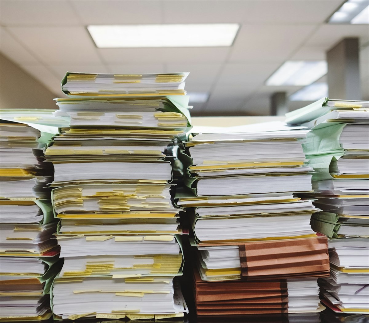Towering stacks of unsorted paperwork and tabbed files piled on an office desk